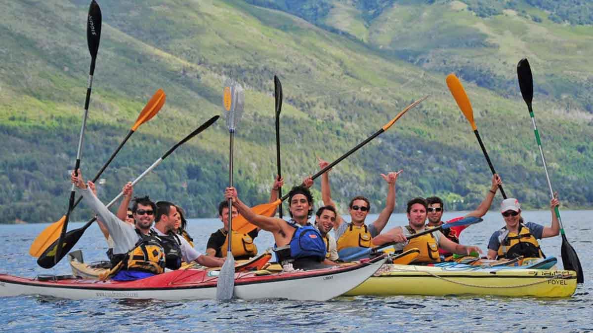 Un grupo levanta los remos desde dos kayaks de travesía en el lago, con la montaña boscosa detrás